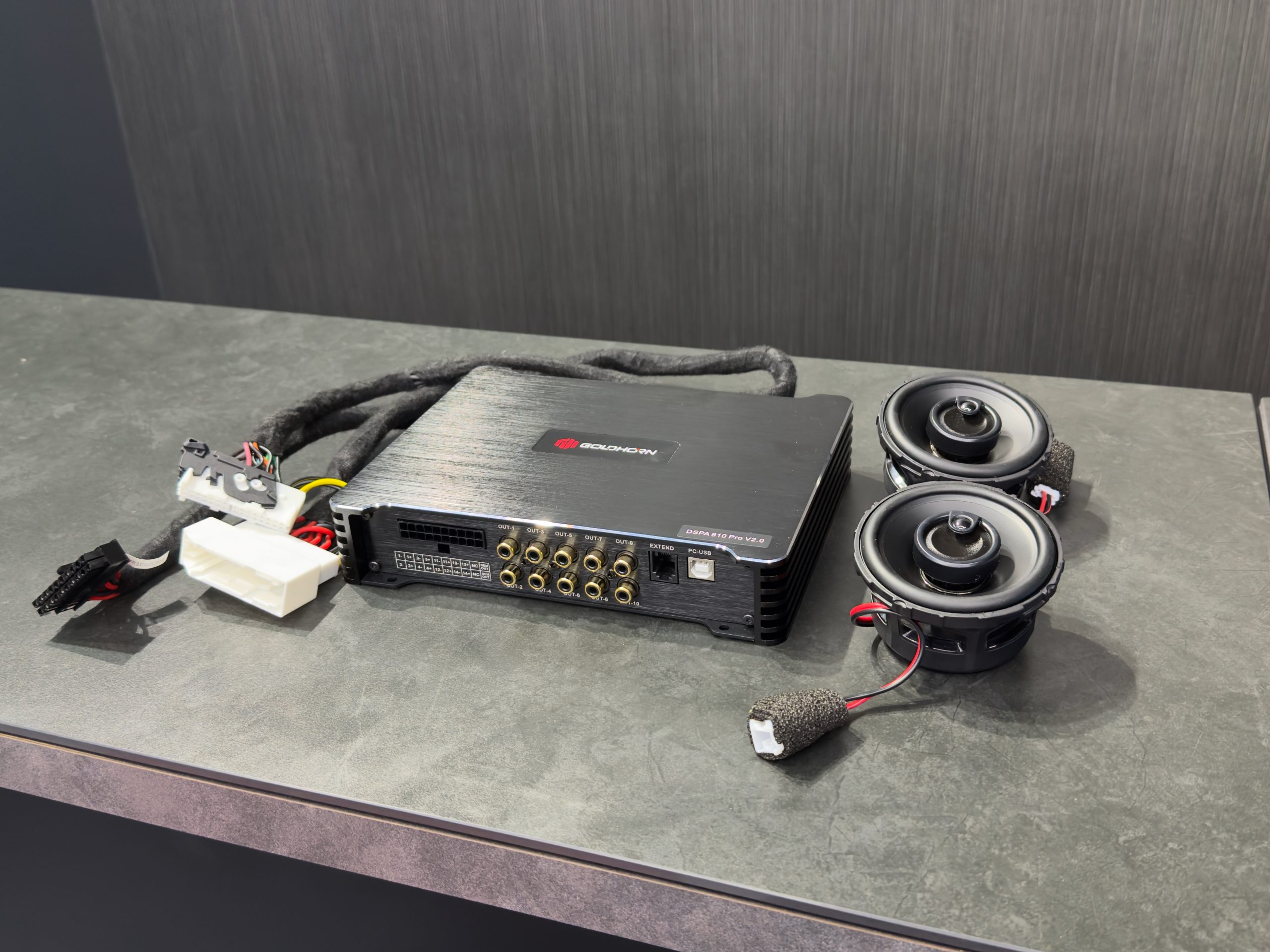 GOLDHORNのDSP、カプラー付きハーネス、2個のスピーカーを作業台に並べた写真